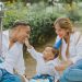 A joyful family celebrating their child's first birthday outdoors with cake and balloons.